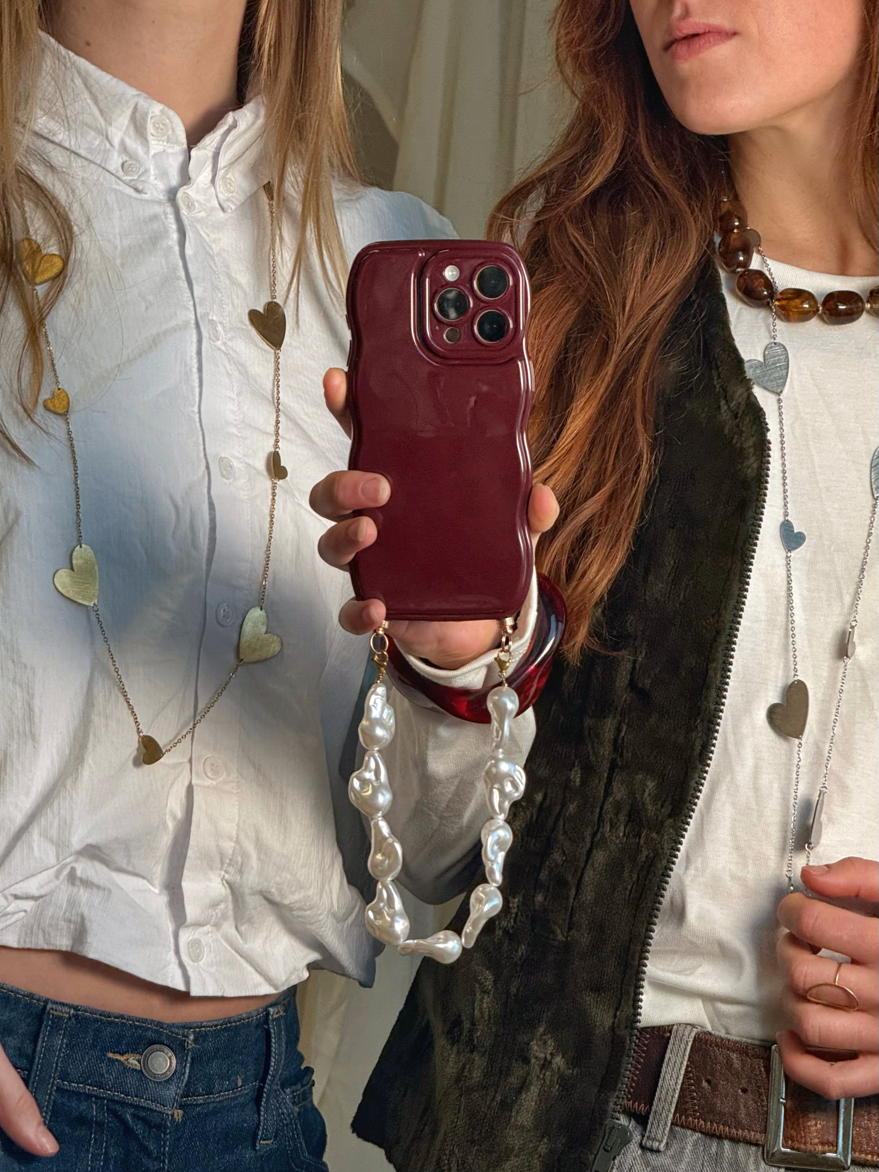 twee meiden met lange hartjes kettingen en een telefoon in het midden met een telefoonkoord van parels